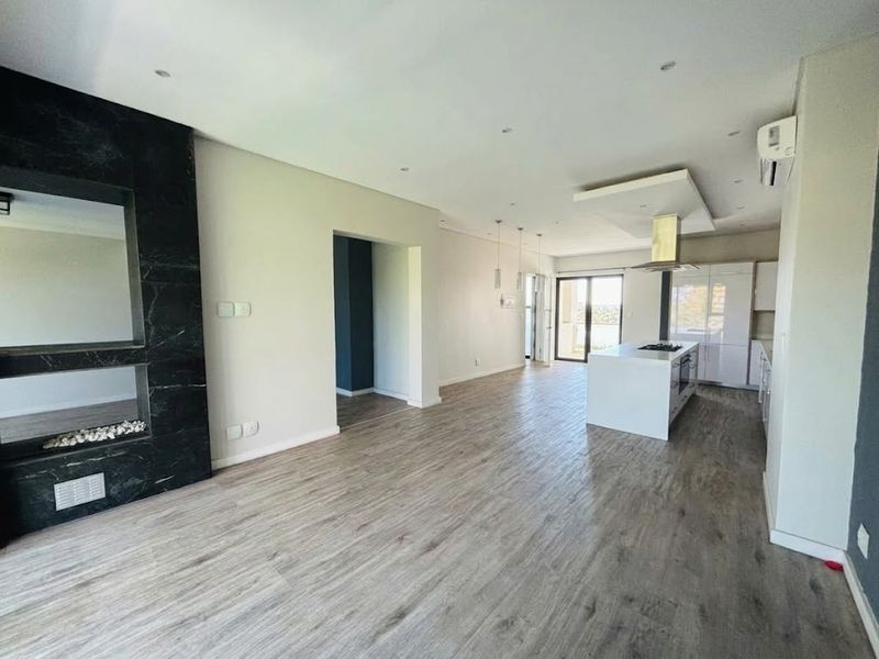 Spacious open-plan living and kitchen area featuring modern laminate flooring, a sleek kitchen island with built-in hob, and a contemporary black marble fireplace feature.
