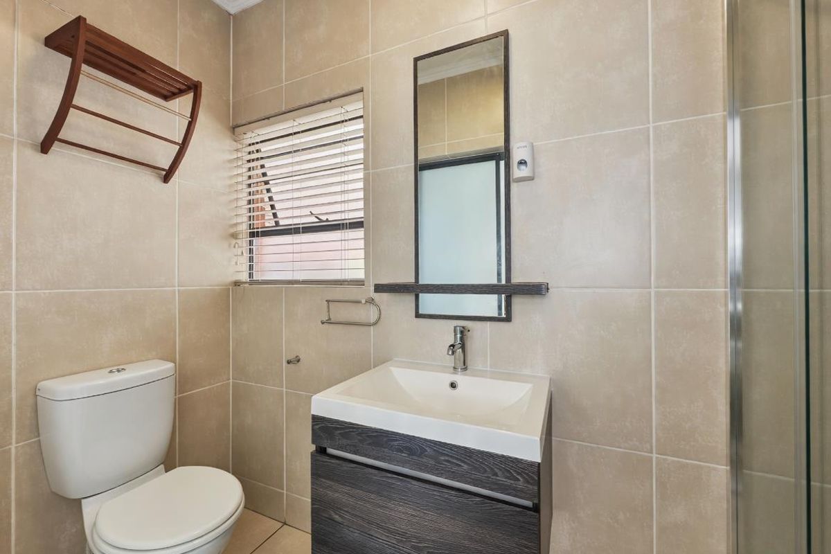 A clean and functional bathroom featuring a modern vanity, wall-mounted mirror, toilet, and a glass-enclosed shower with neutral wall tiling.