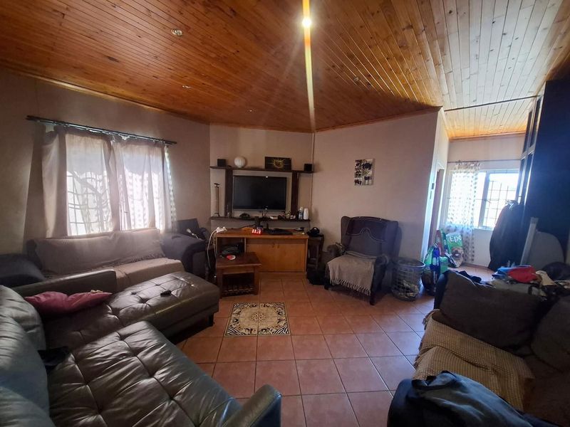 A living room featuring a vaulted timber tongue and groove ceiling, tiled flooring, and a built-in media shelving unit.
