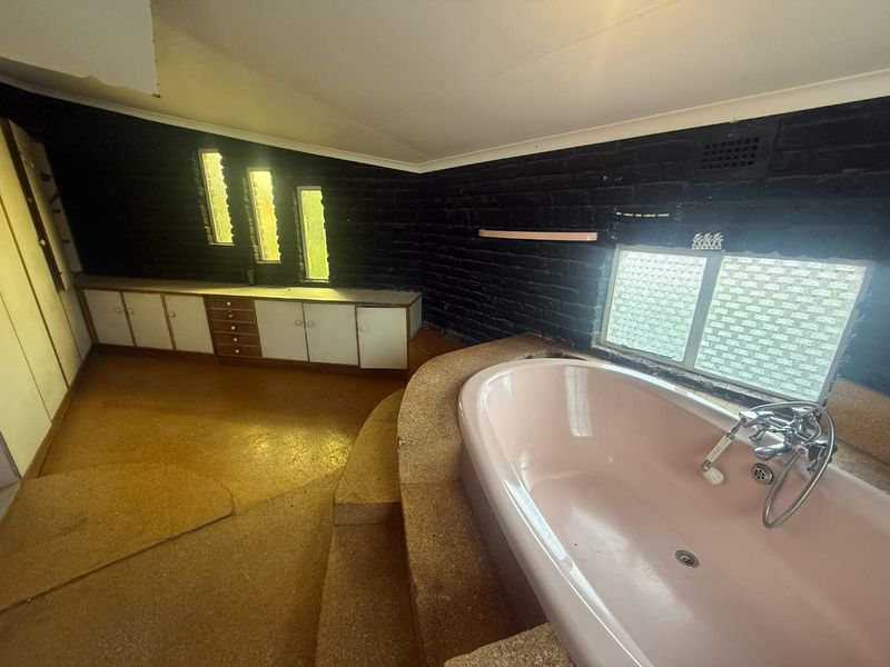 A spacious, dated bathroom featuring a built-in pink bathtub on a raised platform, integrated cabinetry, and textured black brick walls.