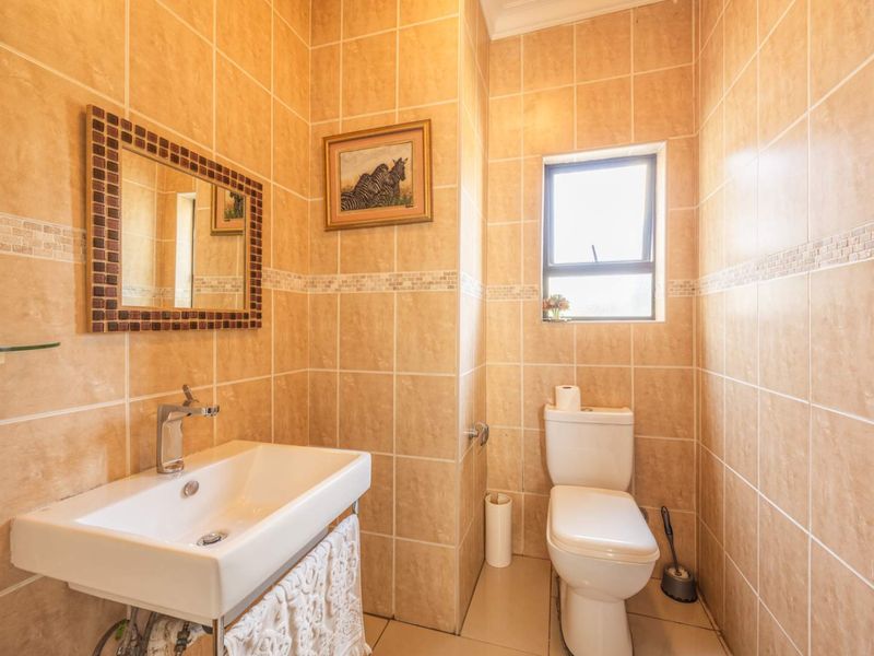 A compact bathroom featuring floor-to-ceiling beige tiling, a wall-mounted basin with chrome fixtures, and a standard ceramic toilet.