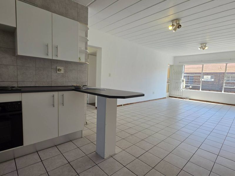Open-plan living and kitchen area featuring tiled flooring, built-in cabinetry, and a breakfast bar, offering a bright and functional space.
