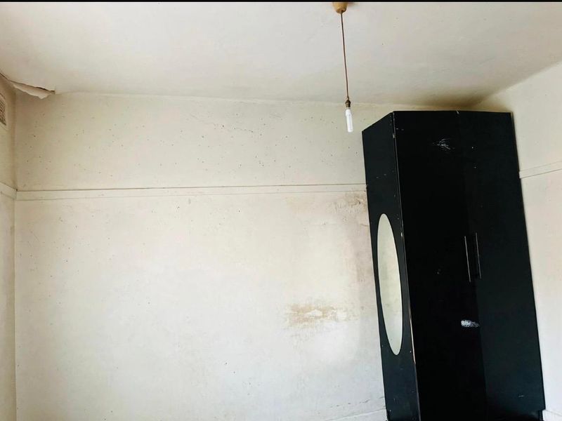 A bedroom space requiring renovation, featuring visible wall and ceiling damage, a picture rail, and a ventilation grille.