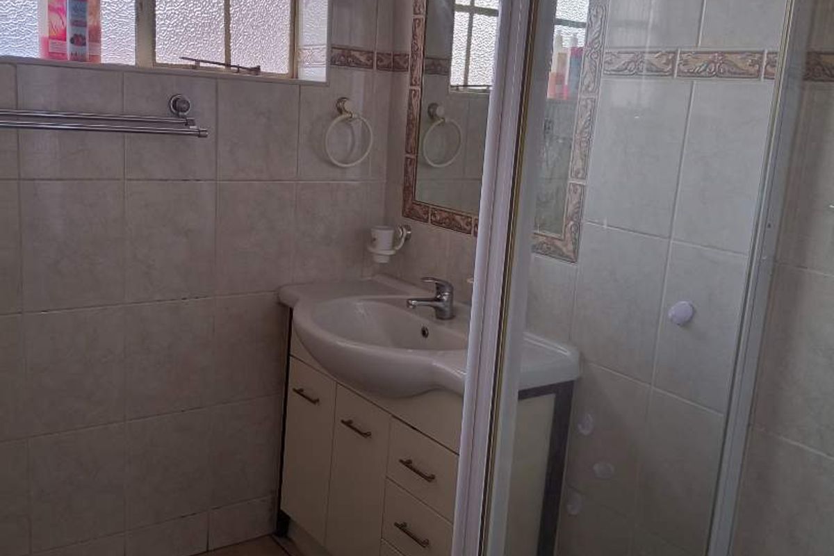 A functional bathroom featuring a vanity cabinet with basin, a shower enclosure, and tiled finishes throughout.