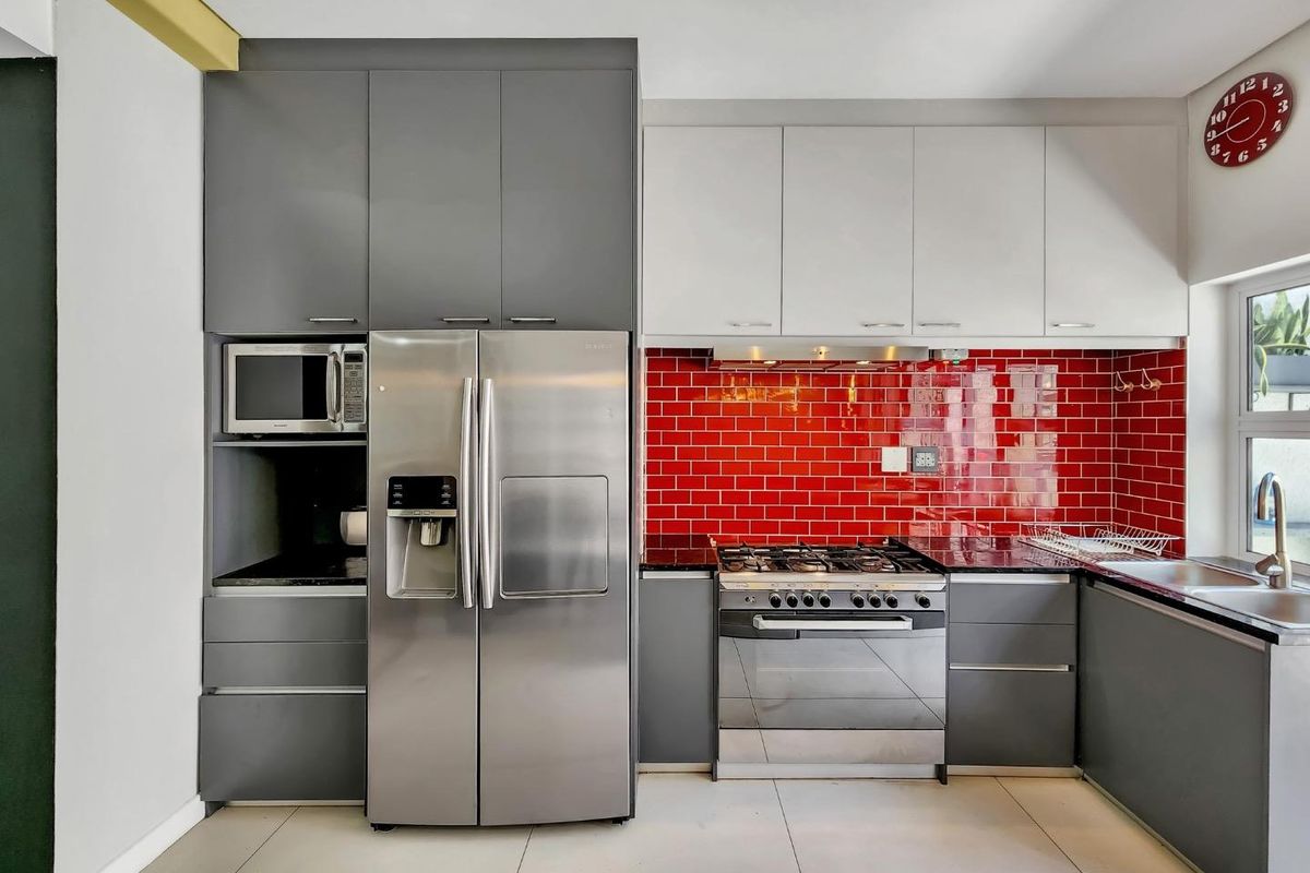Modern kitchen featuring two-tone cabinetry, a striking red subway tile backsplash, granite countertops, and integrated stainless steel appliances.