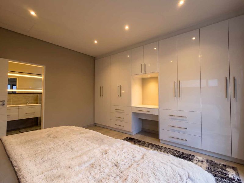 Spacious bedroom featuring extensive high-gloss built-in cabinetry with an integrated vanity station, recessed lighting, and direct access to an en-suite bathroom.