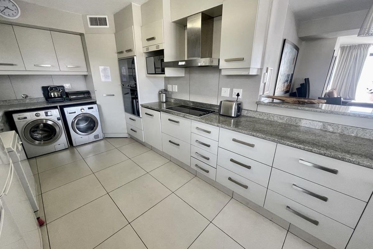 Modern kitchen featuring granite countertops, built-in oven, extractor fan, and integrated laundry appliances with ample cabinetry for storage.