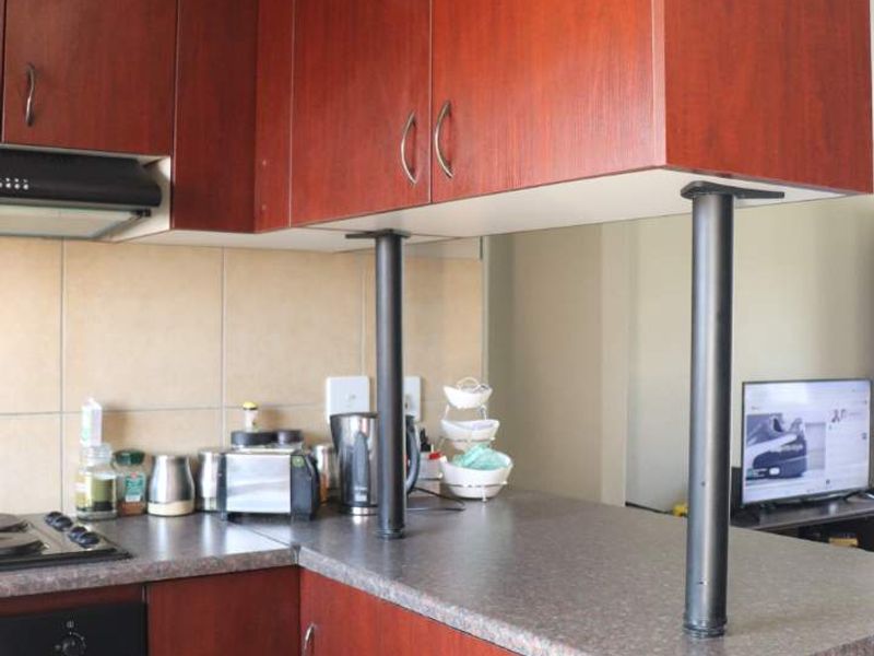 A functional kitchen featuring dark wood-look cabinetry, laminate countertops, a built-in oven, hob, and a breakfast bar with support pillars.