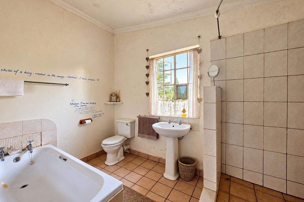 A dated bathroom featuring a pedestal basin, built-in bathtub, and separate tiled shower enclosure, requiring cosmetic updates and ceiling repairs.
