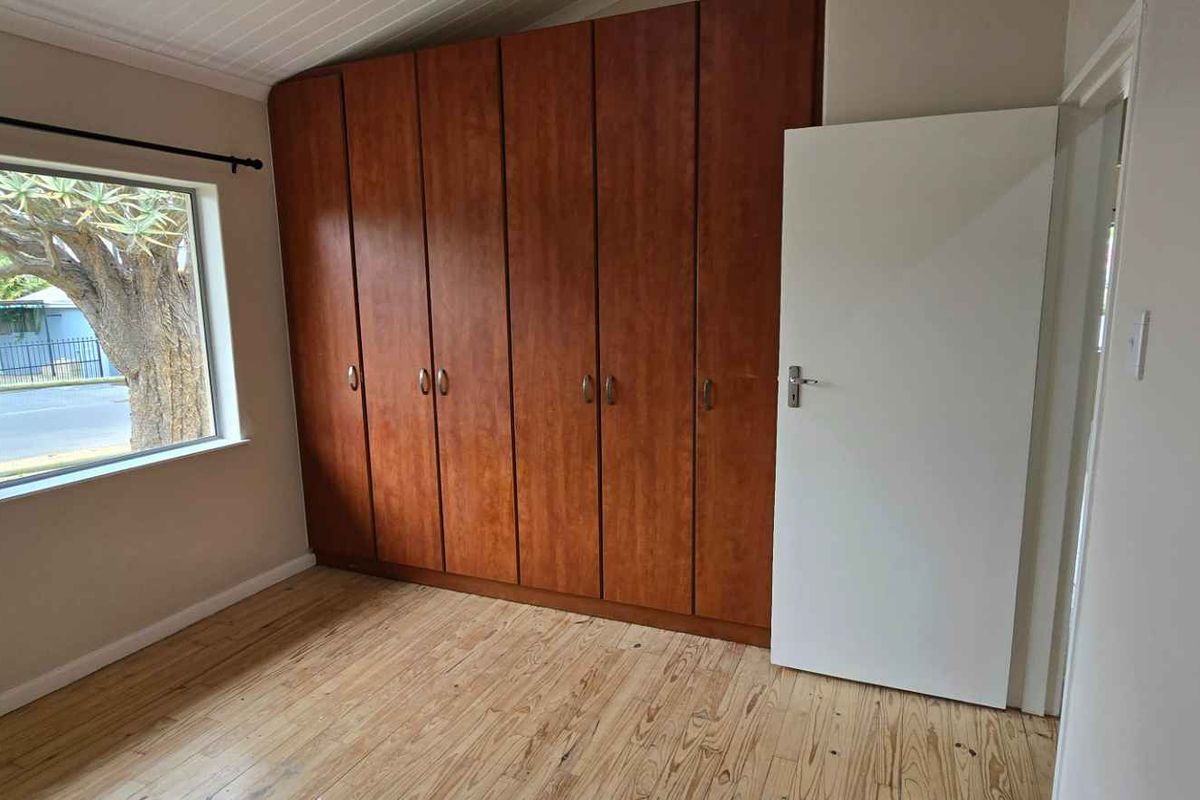 A bedroom featuring built-in wooden cabinetry, timber flooring, and a large window providing natural light.
