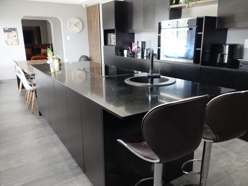 Modern kitchen featuring a large black island with integrated hob and sink, sleek cabinetry, built-in oven, and contemporary tiled flooring.