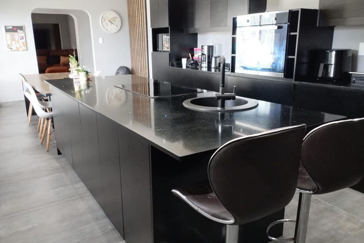 Modern kitchen featuring a large black island with integrated hob and sink, sleek cabinetry, built-in oven, and contemporary tiled flooring.