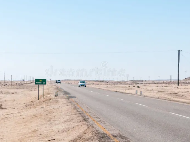 A view of a paved road passing through an arid, undeveloped landscape with utility poles and road signage visible.