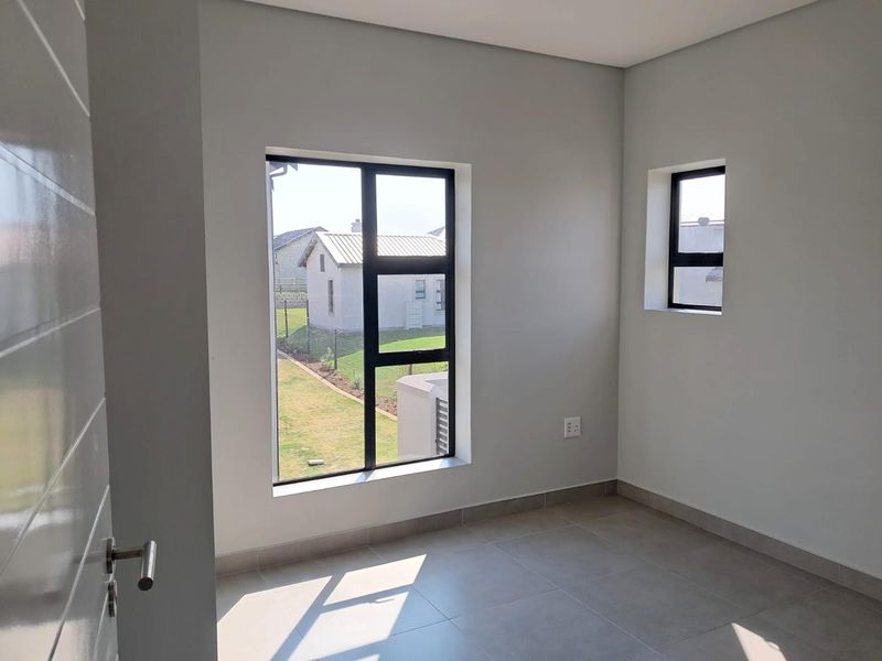 A bright, empty bedroom featuring neutral tiled flooring, modern aluminium-framed windows, and clean, freshly painted walls.