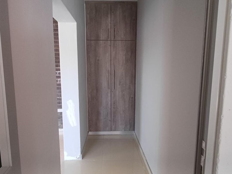 A functional hallway featuring neutral tiled flooring and a modern wood-finish built-in cupboard, providing convenient storage space.