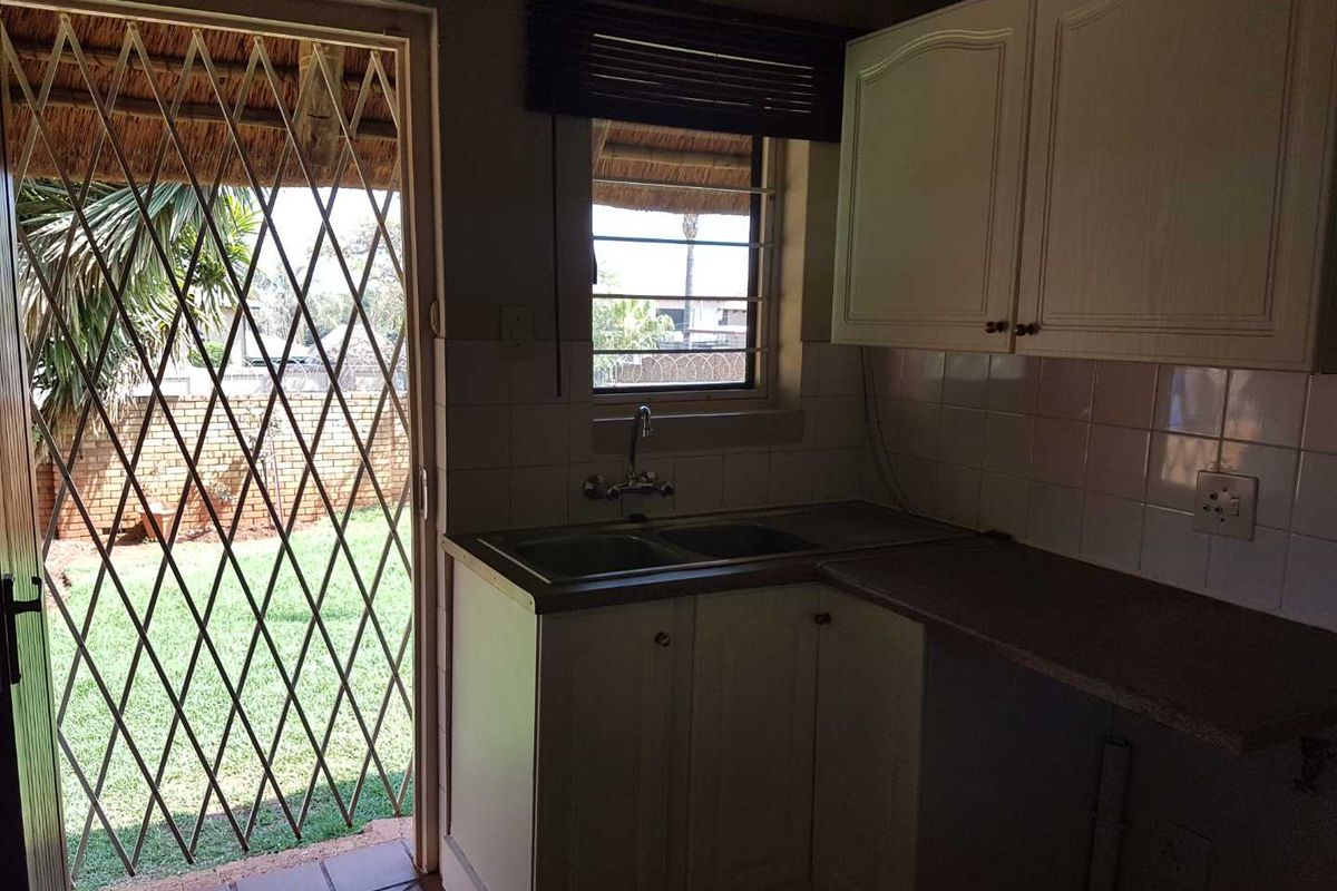A functional kitchen area featuring built-in cabinetry, a double sink, and direct access to the garden through a security-gated door.