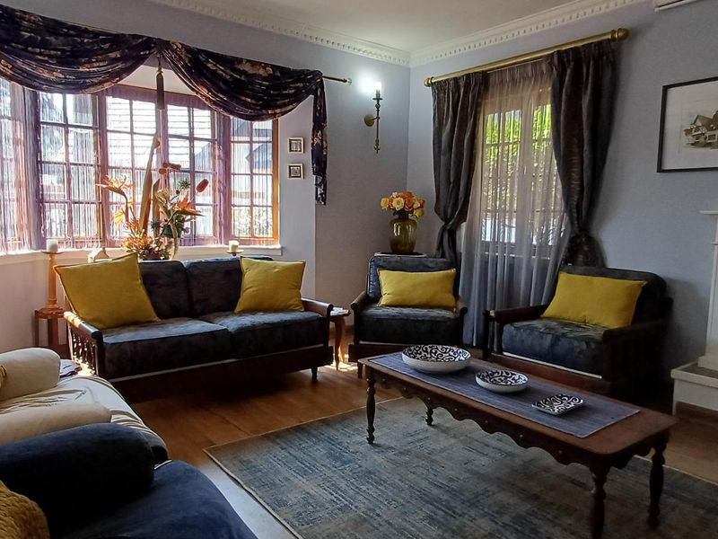 A cozy living room featuring timber flooring, a classic fireplace with a mantelpiece, and a large bay window providing natural light.