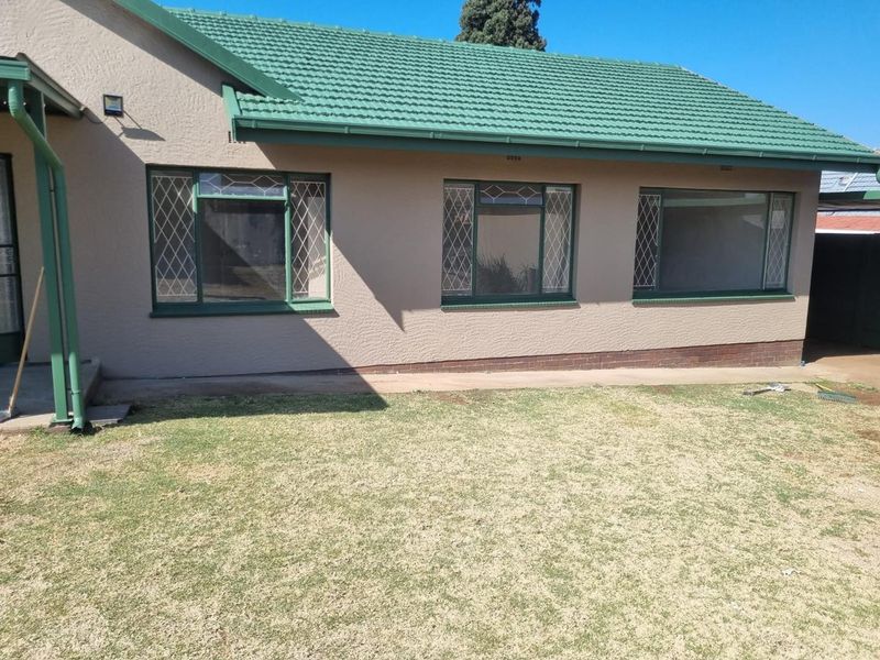 Rear view of the house featuring a tiled roof, diamond pattern security bars on windows, and a concrete pathway leading along the exterior wall.