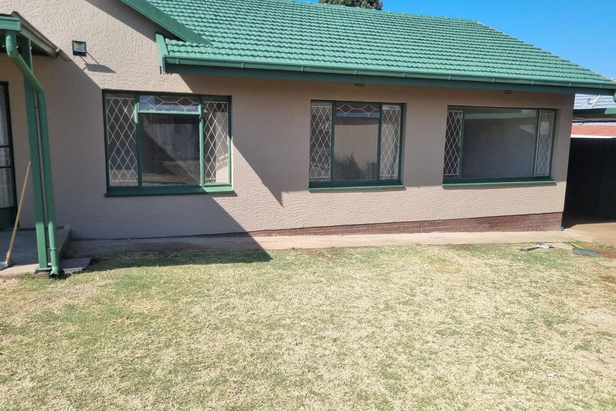 Rear view of the house featuring a tiled roof, diamond pattern security bars on windows, and a concrete pathway leading along the exterior wall.