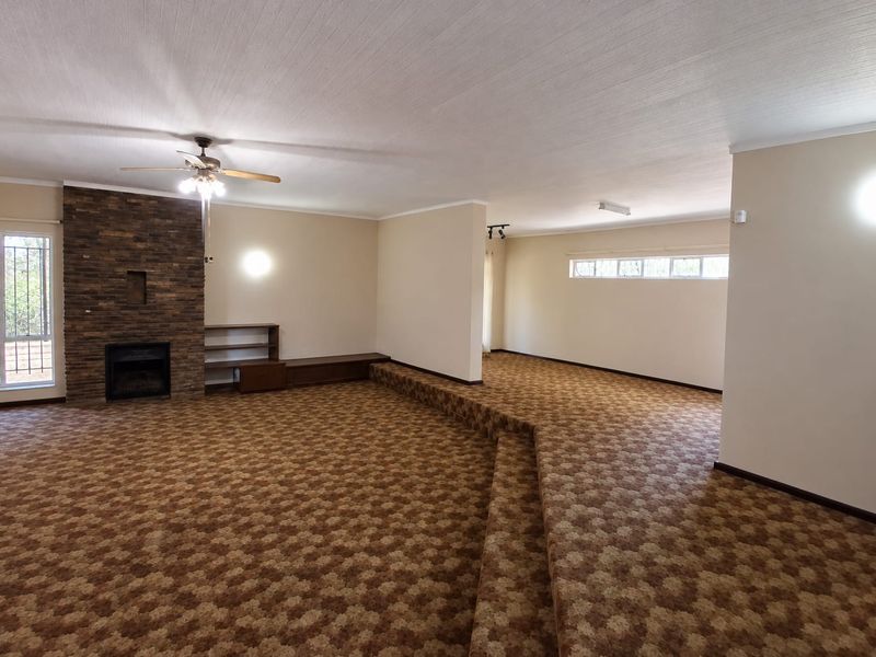 Spacious living area featuring a prominent stone fireplace, built-in shelving, and a unique sunken floor design, offering a versatile layout for renovation.
