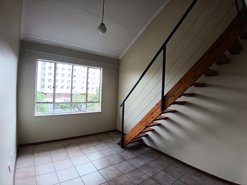 An empty living area featuring tiled flooring, a timber staircase with a metal handrail, and a large window providing natural light.