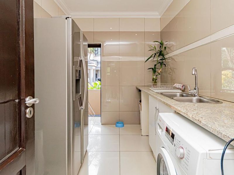 A functional laundry room featuring granite countertops, a double bowl stainless steel sink, and full-height wall tiling.