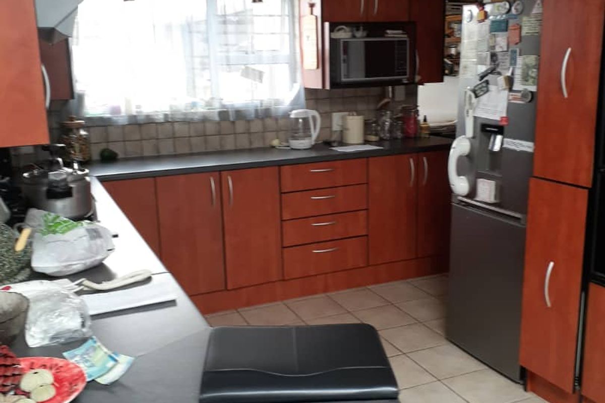 A functional kitchen featuring wood-tone cabinetry, laminate countertops, tiled flooring, and built-in storage space, offering a practical layout for daily meal preparation.