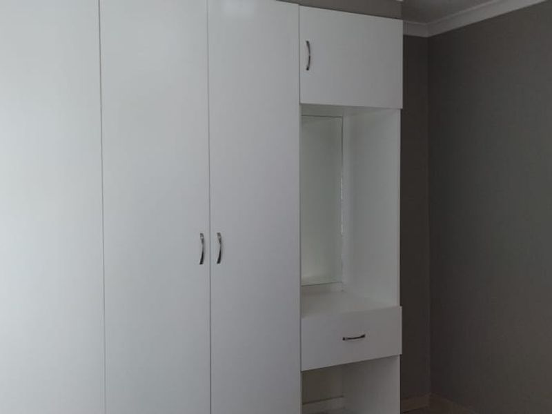 A bedroom featuring a clean, white built-in wardrobe with an integrated vanity unit and mirror, set against neutral grey walls.