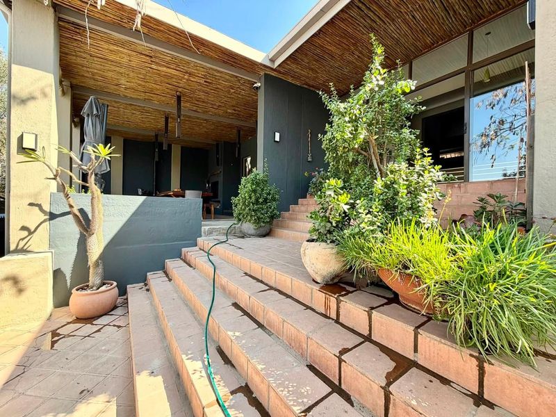 A covered outdoor patio area featuring a thatched roof, tiled staircase, and large sliding glass doors leading into the main living space.