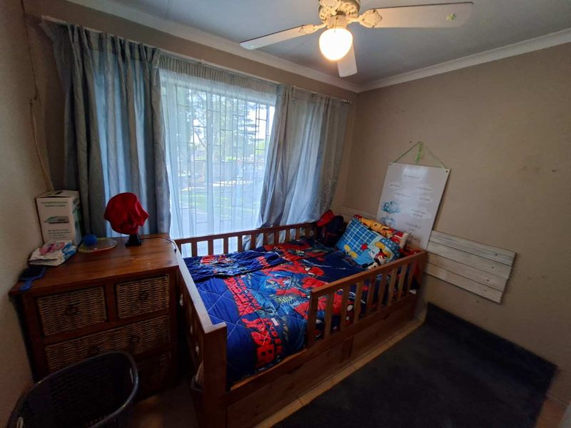A bedroom featuring tiled flooring, a ceiling fan, and a window fitted with security bars.