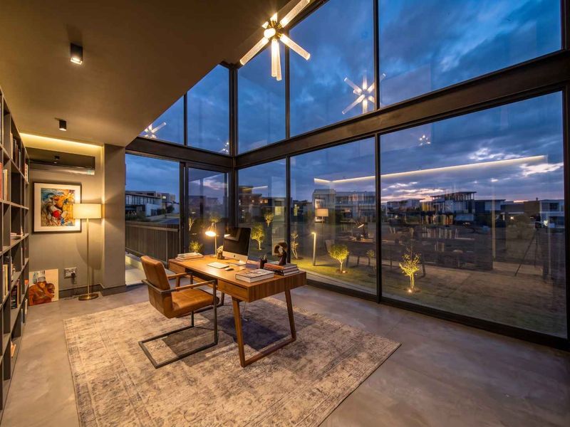 Modern home office featuring expansive floor-to-ceiling glass walls, built-in shelving, and polished concrete floors with views of the surrounding estate.