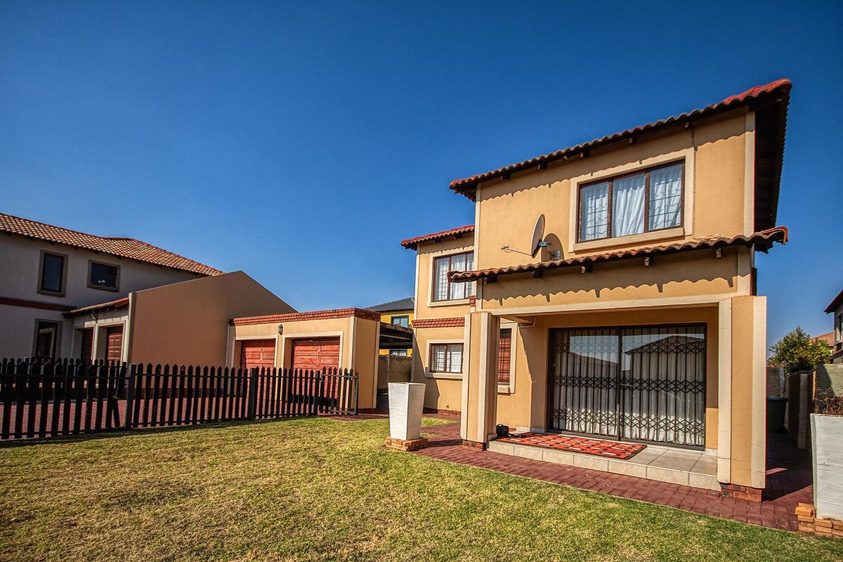 Rear view of a two-story house featuring a paved patio, a small lawn, and a double garage with wooden doors.