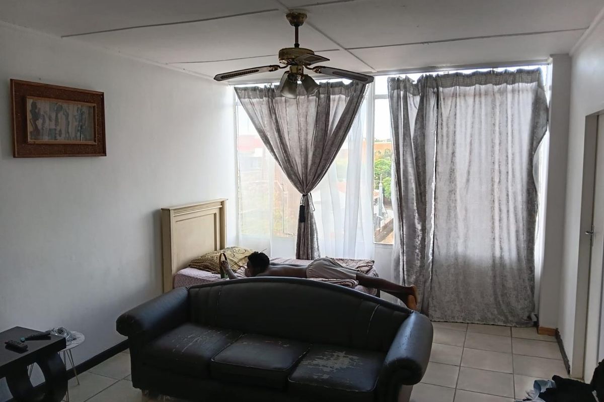 A bedroom featuring tiled flooring, a ceiling fan, and large windows allowing natural light. The space requires cosmetic updates to improve its overall condition.
