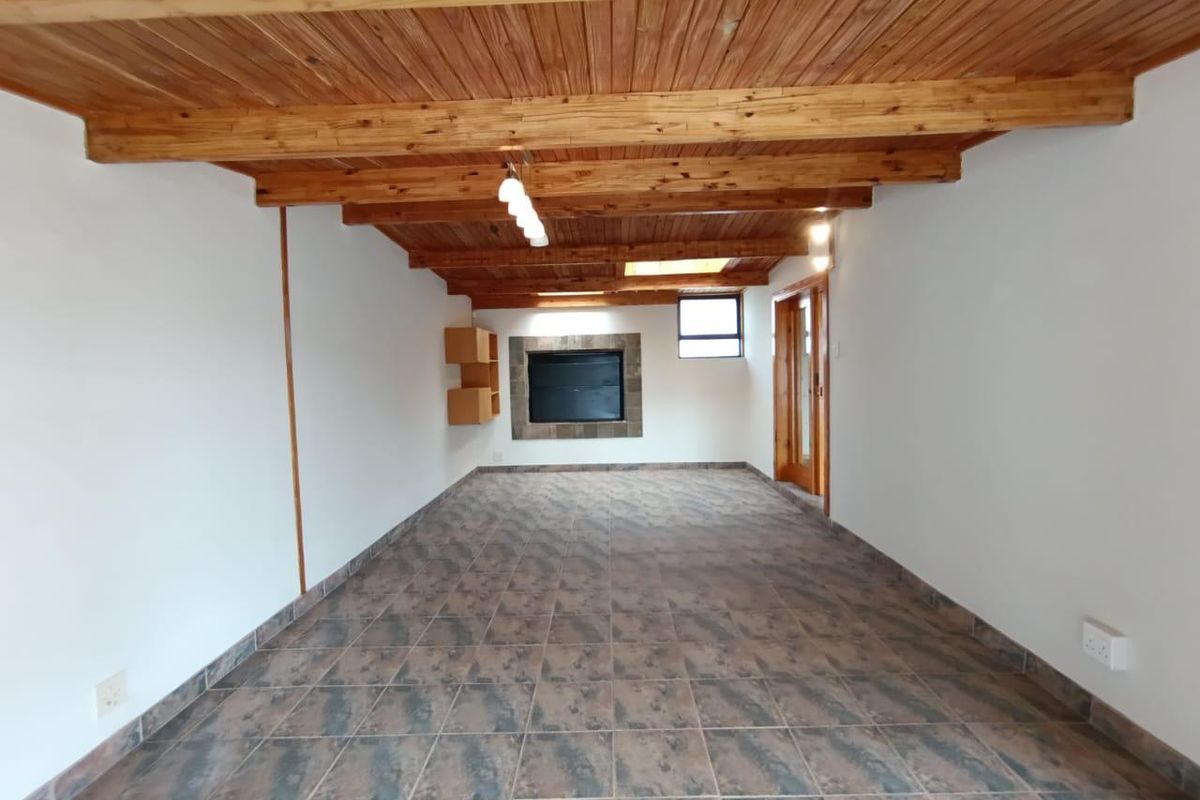 An empty living room featuring exposed timber beam ceilings, tiled flooring, a built-in fireplace, and a skylight, offering a rustic and spacious interior.
