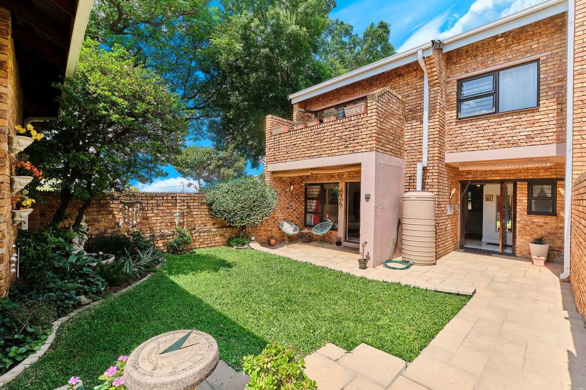 A private rear garden featuring a paved patio area, established lawn, and brick townhouse facade with a balcony and water tank.