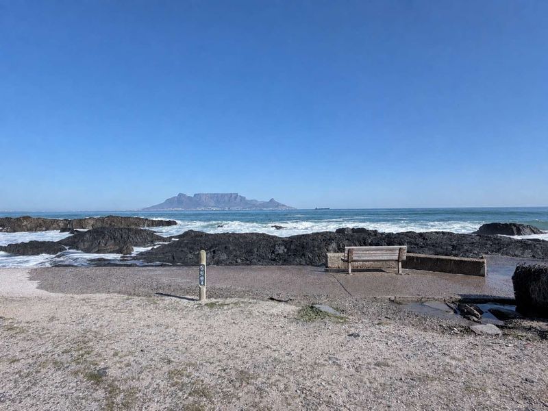 A scenic view of the coastline featuring rocky outcrops and a distant mountain range under a clear blue sky.