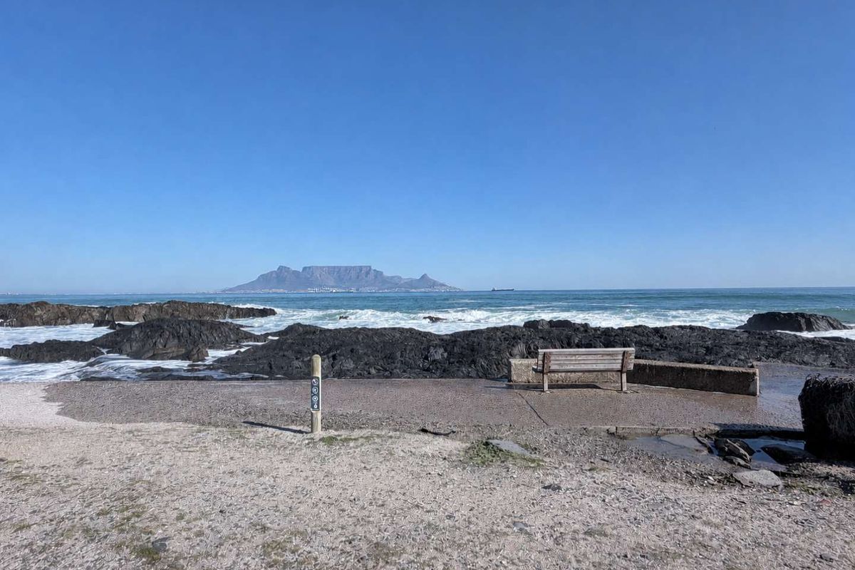A scenic view of the coastline featuring rocky outcrops and a distant mountain range under a clear blue sky.