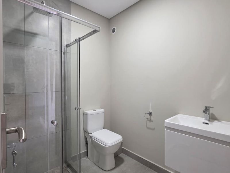 Modern bathroom featuring a glass-enclosed shower with rain shower head, wall-mounted toilet, and a sleek vanity basin with chrome fixtures.
