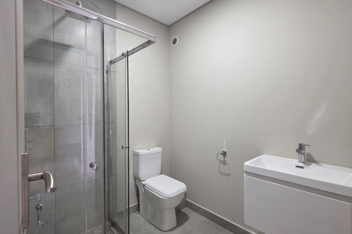 Modern bathroom featuring a glass-enclosed shower with rain shower head, wall-mounted toilet, and a sleek vanity basin with chrome fixtures.