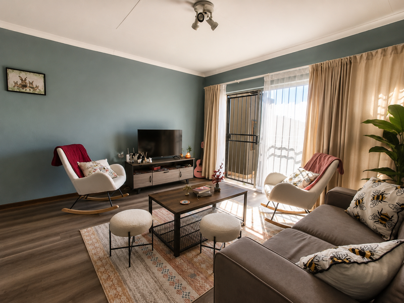 A well-lit living room featuring modern laminate flooring, a sliding glass door with security gate, and neutral wall tones.
