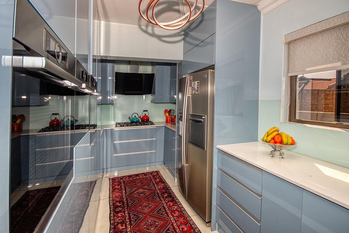 Modern kitchen featuring high-gloss blue cabinetry, stone countertops, built-in oven, gas hob, extractor fan, and tiled flooring.