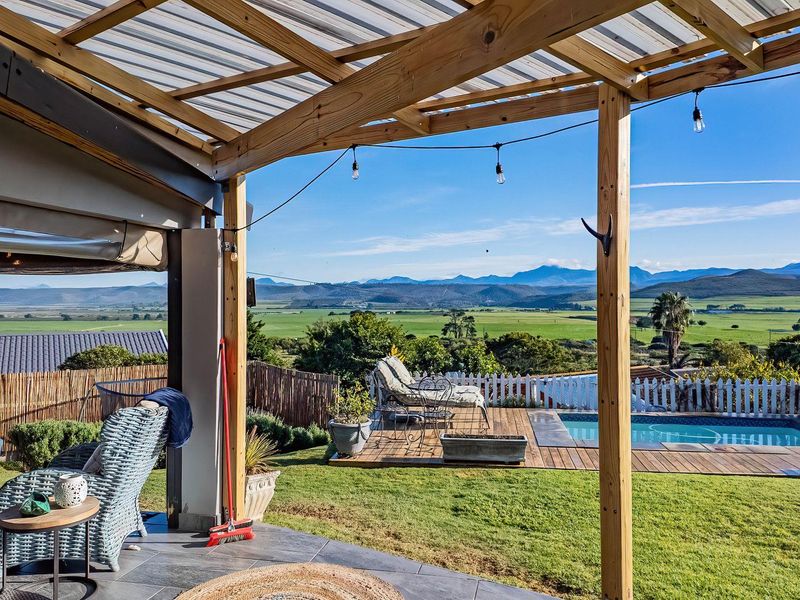 Covered patio featuring a timber pergola and tiled flooring, overlooking a swimming pool, timber deck, and expansive mountain landscape views.