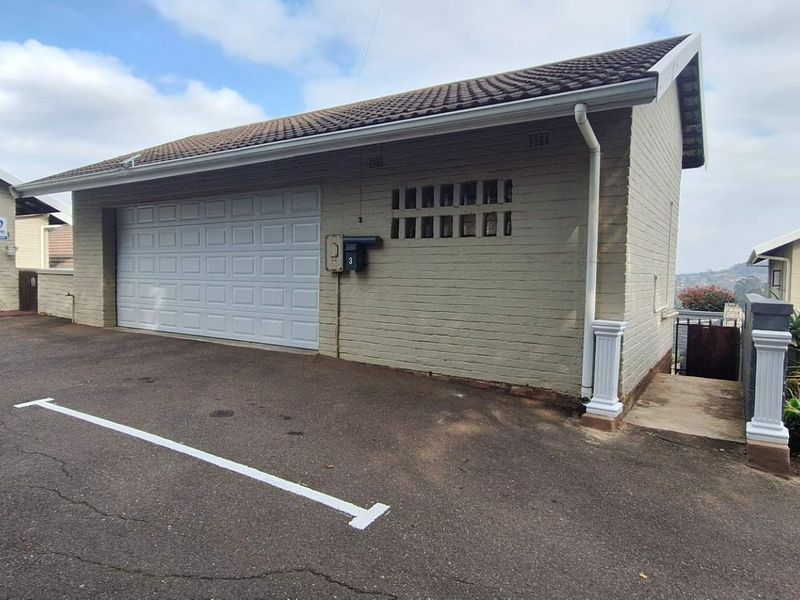 Exterior view of a single-car garage featuring a white sectional door, brick construction, and a paved driveway area.