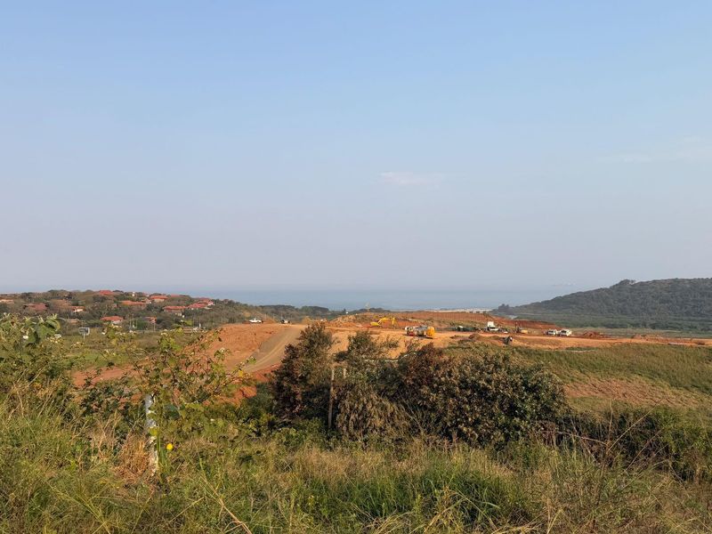 An elevated view of a large, undeveloped residential land plot featuring coastal landscape and distant ocean views.