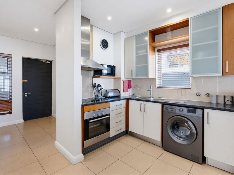 A compact, functional kitchen featuring modern cabinetry, granite countertops, built-in oven, extractor fan, and integrated laundry plumbing, finished with neutral floor tiles.