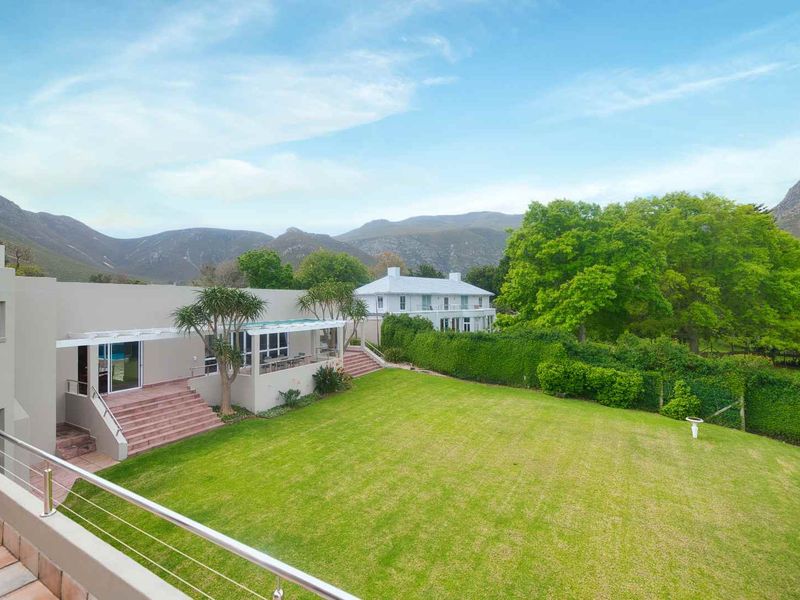 Spacious rear garden featuring a well-maintained lawn, tiled patio area with stainless steel balustrades, and scenic mountain views.