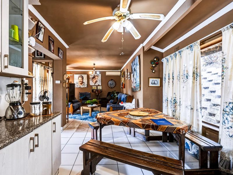 Open-plan living and kitchen area featuring tiled flooring, ceiling fan, and built-in cabinetry with granite countertops.
