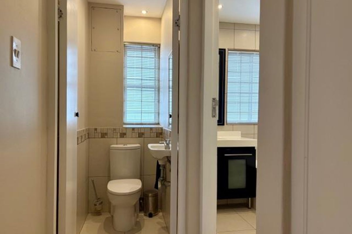 A functional bathroom featuring a toilet, pedestal basin, and a separate vanity area with tiled finishes and natural light from venetian blinds.