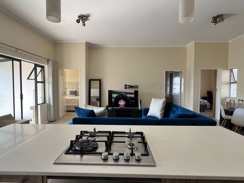 Spacious open-plan living area featuring a modern kitchen island with a gas hob, flowing seamlessly into the lounge with access to a balcony.