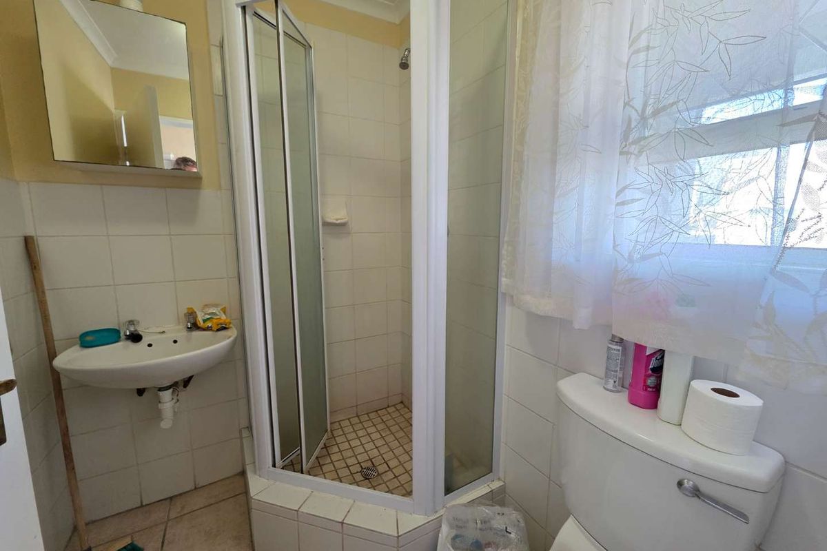 A compact bathroom featuring a corner shower enclosure, wall-mounted basin, and toilet with tiled finishes throughout.
